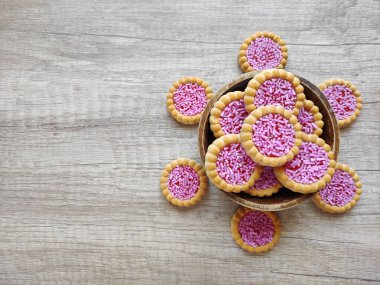 Yuvarlak pişmiş tatlı bisküviler, parlak kırmızı dolgu ve pembe pasta parçacıkları, dekoratif bir tabakta