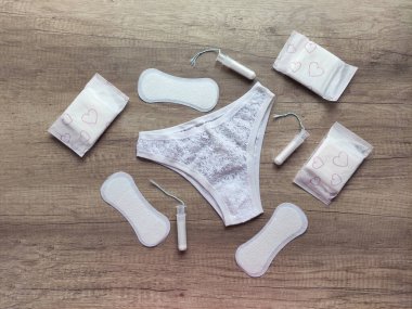 Ahşap arka planda kadın iç çamaşırı, hijyenik pedler ve tamponlar.