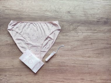 Ahşap arka planda kadın iç çamaşırı, hijyenik pedler ve tamponlar.
