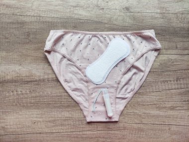 Ahşap arka planda kadın iç çamaşırı, hijyenik pedler ve tamponlar.