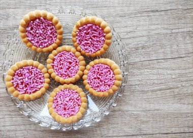  Yuvarlak pişmiş tatlı bisküviler, parlak kırmızı dolgu ve pembe pasta parçacıkları, dekoratif bir tabakta