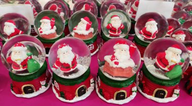 İçinde Noel Baba figürleri olan cam toplar, kırmızı üzerinde kar taneleri ve Noel Baba 'nın küçük resimleriyle süslenmiş.