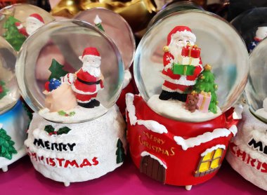 İçinde Noel Baba figürleri olan cam toplar, kırmızı üzerinde kar taneleri ve Noel Baba 'nın küçük resimleriyle süslenmiş.