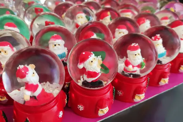 İçinde Noel Baba figürleri olan cam toplar, kırmızı üzerinde kar taneleri ve Noel Baba 'nın küçük resimleriyle süslenmiş.