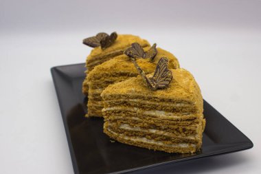 Üzerinde siyah bir tabakta çikolata parçacıkları olan üç kat ballı pasta..