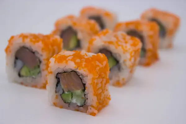 stock image A close-up image featuring a diagonal line of California roll sushi pieces, each one topped with a generous layer of vibrant orange masago. The rolls are expertly sliced to reveal the harmonious filling of tender crab meat, creamy avocado, and crisp 