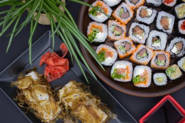 Resim, birbirine zıt şekil ve dokulara sahip iki tabağın yer aldığı bir suşi ziyafetini ustaca yakalıyor. Siyah dikdörtgen tabakta, üzerinde bonito taneleri olan suşi ruloları turşulu zencefil turşusunun yanında oturur, onların narin pembesi altın tanesiyle tezat oluşturur.