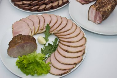 Taze sarımsak, roka ve marulla süslenmiş düzgünce hazırlanmış füme domuz eti tabağı. Ekranda etin zengin, dumanlı tadı ve yumuşak dokusu vurgulanıyor