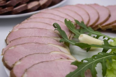 Taze otlar ve sebzelerle süslenmiş, dilimlenmiş güzel bir tabak sosis ve jambon. Lezzetli bir doku ve lezzet karışımı. Bir gurme yemeği için mükemmel..