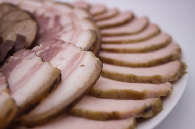 İnce dilimlenmiş domuz eti göbeğinin detaylı bir yakın çekimi, zengin mermerini ve dumanlı dokusunu vurguluyor. Zanaatkar şarküterinin kalitesini ve lezzetini göstermek için mükemmel bir görüntü..