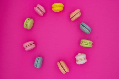 Parlak pembe arka planda dairesel bir desen oluşturan canlı bir badem kurabiyesi düzeni. Makaronlar çeşitli renklerde, pembe, yeşil, mavi, sarı, şeftali ve beyaz gibi..