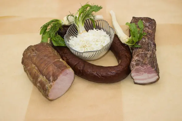 stock image An arrangement of smoked meats with fresh horseradish roots and greens. Includes a sliced smoked pork loin and sausage, complemented by a bowl of grated horseradish, highlighting a rustic culinary tradition.