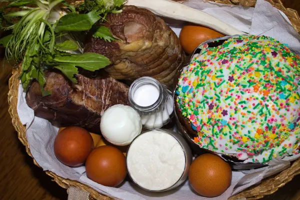 stock image A beautifully arranged Easter basket filled with traditional festive foods. Includes vibrant Easter eggs, a decorated Easter bread with sprinkles, smoked meats, fresh greens, and a glass jar of salt.