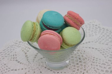 Cam bir kâseye yerleştirilmiş çeşitli pastel renkli makaronlar, pembe, yeşil ve mavi renkler sergiliyorlar. Narin, çıtır çıtır kabuklar ve kremalı dolgular zarif ve davetkar bir ziyafet yaratır..