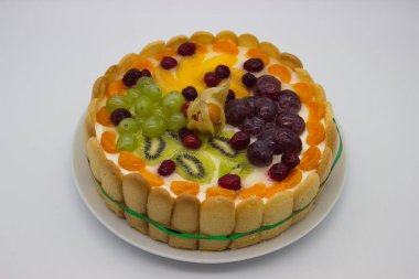 Canlı bir meyveli tartın bu yakın çekimi bir dizi sulu böğürtlen, üzüm, kivi ve kremalı dolgu üzerine dizilmiş bitki örtüsünü ön plana çıkarıyor. Jöle taze, ışıl ışıl bir doku ekler. Tatlının görsel çekiciliğini arttırır..