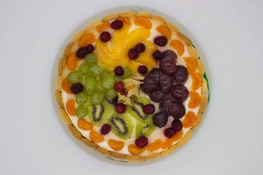 Canlı bir meyveli tartın bu yakın çekimi bir dizi sulu böğürtlen, üzüm, kivi ve kremalı dolgu üzerine dizilmiş bitki örtüsünü ön plana çıkarıyor. Jöle taze, ışıl ışıl bir doku ekler. Tatlının görsel çekiciliğini arttırır..