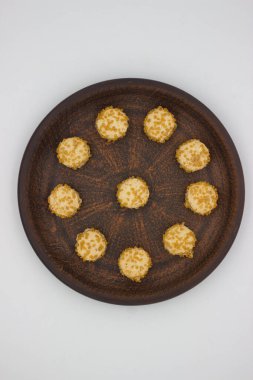 Kırsal seramik tabakta daire şeklinde dizilmiş mini tatlı kurabiyelerinin yukarıdan aşağı görüntüsü. Her kurabiye ezilmiş fındıkla kaplıdır, lezzetli bir atıştırmalık yaratır..