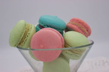 Cam bir kâseye yerleştirilmiş çeşitli pastel renkli makaronlar, pembe, yeşil ve mavi renkler sergiliyorlar. Narin, çıtır çıtır kabuklar ve kremalı dolgular zarif ve davetkar bir ziyafet yaratır..