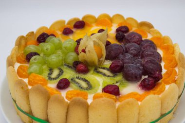 Canlı bir meyveli tartın bu yakın çekimi bir dizi sulu böğürtlen, üzüm, kivi ve kremalı dolgu üzerine dizilmiş bitki örtüsünü ön plana çıkarıyor. Jöle taze, ışıl ışıl bir doku ekler. Tatlının görsel çekiciliğini arttırır..