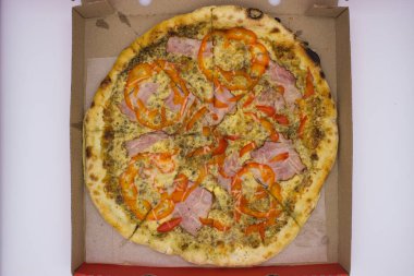 Üzerinde jambon ve kırmızı dolma biber dilimleri olan karton bir kutuda lezzetli bir pizza. Altın hamuru ve zengin malzemeler onu iştah açıcı bir yemek yapar. Her pizzacı için mükemmeldir..