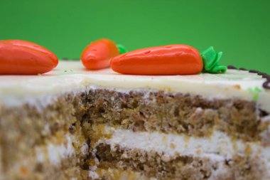 Krema kaplı havuçlu kekin detaylı bir yakın plan görüntüsü nemli katmanlar ve üzerine badem ezmesi havuç süslemeleri sergileniyor..