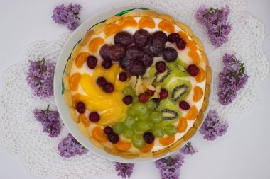 Canlı bir meyveli tartın bu yakın çekimi bir dizi sulu böğürtlen, üzüm, kivi ve kremalı dolgu üzerine dizilmiş bitki örtüsünü ön plana çıkarıyor. Jöle taze, ışıl ışıl bir doku ekler. Tatlının görsel çekiciliğini arttırır..