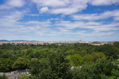 Çarpıcı bir şehir manzarası, canlı mavi gökyüzünün altında yemyeşil yeşilliklerle çevrili, mimari ve doğal güzellikleri uyum içinde sergiliyor..