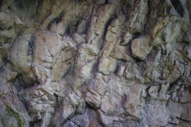 Görünür çatlakları ve çatlakları olan, doğal jeolojik desenleri ve dokuları olan engebeli bir kaya yüzeyinin detaylı bir yakın çekimi..