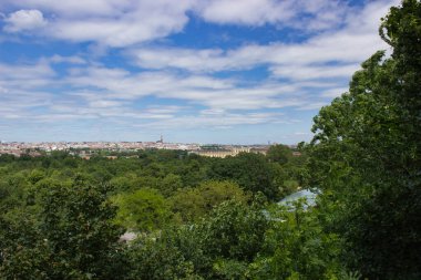 Çarpıcı bir şehir manzarası, canlı mavi gökyüzünün altında yemyeşil yeşilliklerle çevrili, mimari ve doğal güzellikleri uyum içinde sergiliyor..