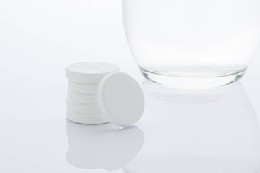 Aspirinler bir bardak suyun yanında küçük bir sütunda gruplandırılmış. Beyaz arkaplan.