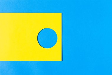 Abstract geometric composition formed by a yellow cardboard with a circle on a blue background.