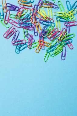 Set of multicolored paper clips on blue background. Copy space.
