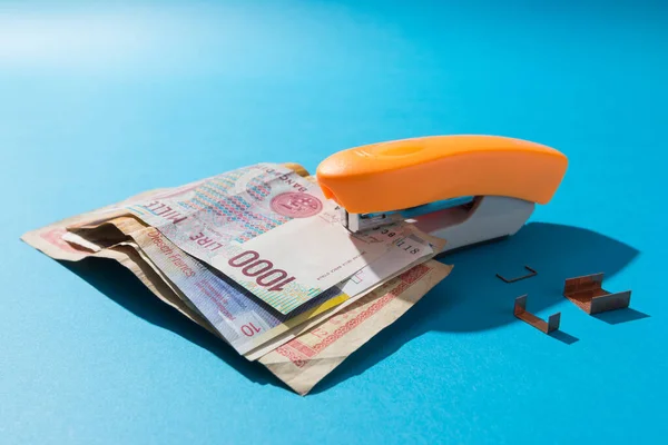 Orange stapler stapling some old international bills. Money saving concept.