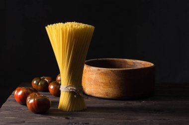 Some tomatoes and a bunch of spaghetti arranged vertically on an antique table. Dark background.