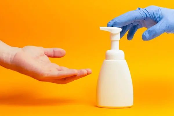 Bir elinde ameliyat eldiveni olan bir el jel kutusuna basmaya hazır, diğeri de eldivensiz eldiveni almaya hazır. Sağlık ve kişisel temizlik kavramı.