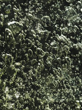 Kabarcıklı, karanlık bir buz dokusunda ışıl ışıl bir güneş ışığı..