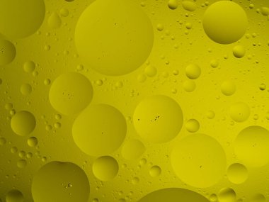 Su yüzeyinde yüzen sarı yağ kabarcıklarının canlı bir makro dokusu, soyut arka planlar için mükemmel..