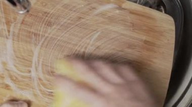 Ellerin yukarıdan aşağıya bambu kesme tahtasını sünger ve sabunla ovalarken sabunlu köpükler yaratırken görünümü.
