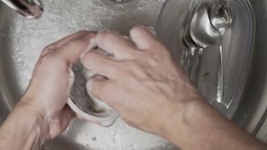 Ellerin yukarıdan aşağıya doğru, lavaboda sabun ve suyla mutfak aletlerini ovalarken, temizliği sağlarken..