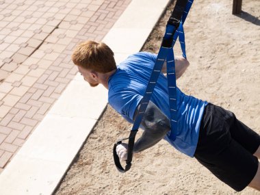 Odaklanmış sporcu, doğal ortamdaki dayanıklılık, dayanıklılık ve genel uygunluğu artırmak için özel ekipmanlar kullanarak, açık havada süspansiyon eğitimi alıyor.