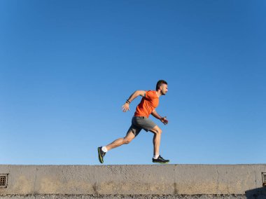 Zinde bir adam beton bir duvara çarpıyor canlı mavi gökyüzüne karşı, somut enerji ve atletizm.