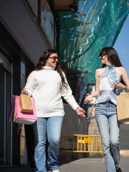 İki mutlu bayan arkadaş alışveriş torbaları taşıyor ve başarılı bir alışveriş çılgınlığından sonra sokakta yürürken sohbet ediyorlar.