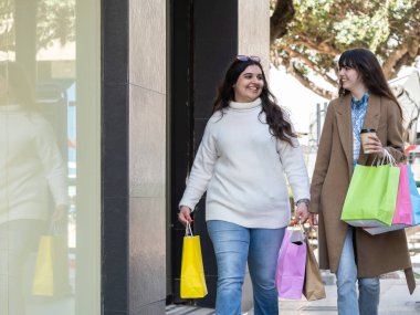 İki kadın keyifli bir alışveriş gününün tadını çıkarıyorlar. Renkli poşetler taşıyorlar, kahve yudumluyorlar ve sokaklarda mutlu bir şekilde sohbet ediyorlar.