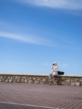 Taş duvarda oturan iş kadını mavi gökyüzünün altında bir telefon görüşmesi yapıyor.