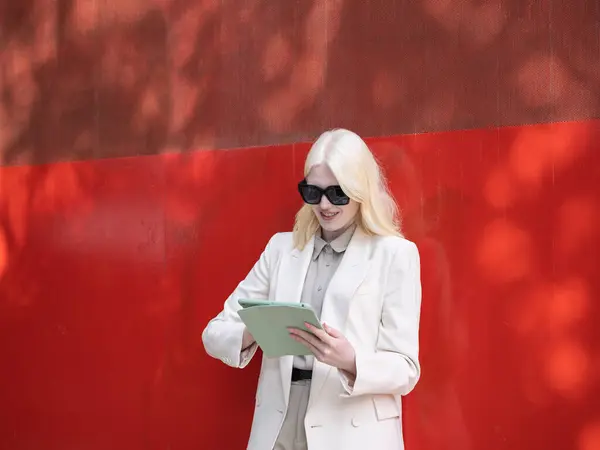 İş kadını kırmızı bir duvarın karşısında gülümserken tablet kullanıyor.