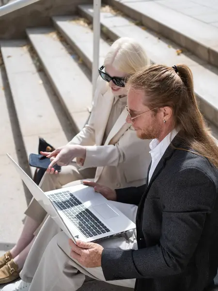 İş ortakları bilgisayar ve akıllı telefon kullanıyor, ofis merdivenlerinde uzaktan çalışıyor.