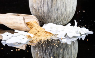 Ahşap kaşıktan taşan hindistan cevizi çiçeği şekeri ve arka planda hindistan cevizi ezmesi. Yansımalı parlak siyah arkaplanda