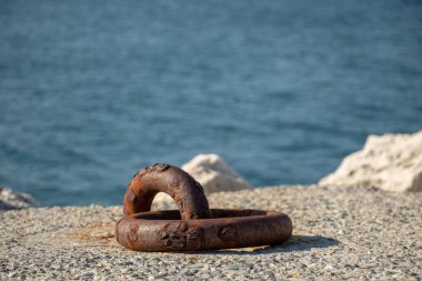 Arka planda deniz olan dalgakıran üzerinde paslı bir tekne için demirleme halkası.