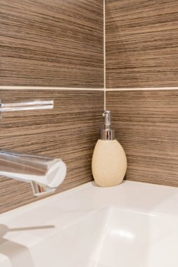 Kahverengi fayanslı duvar ve banyo musluğunun önündeki seramik sabun makinesi.