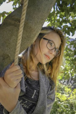 Ağaç portresinin altında bir ip tutan gözlüklü, gülümseyen genç kadın.
